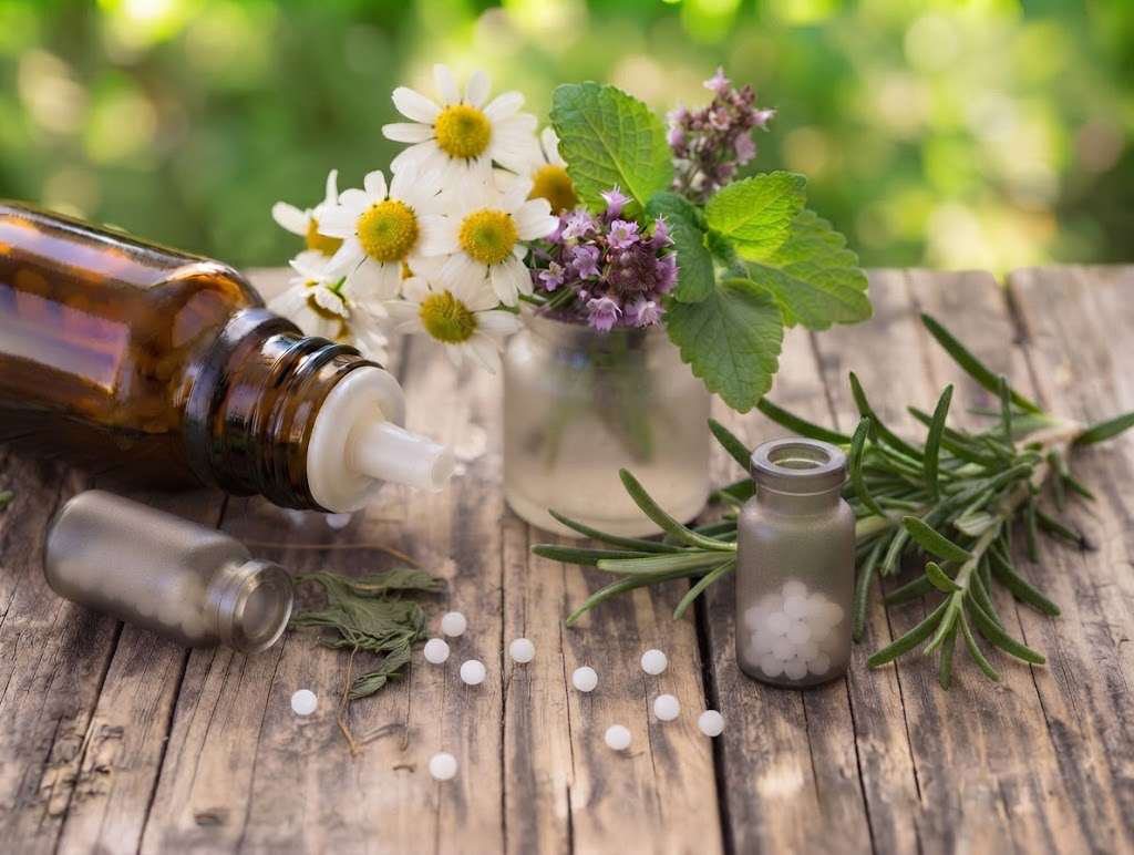 Homöopathische Globuli mit Kräutern und Braunglasflaschen auf Holz